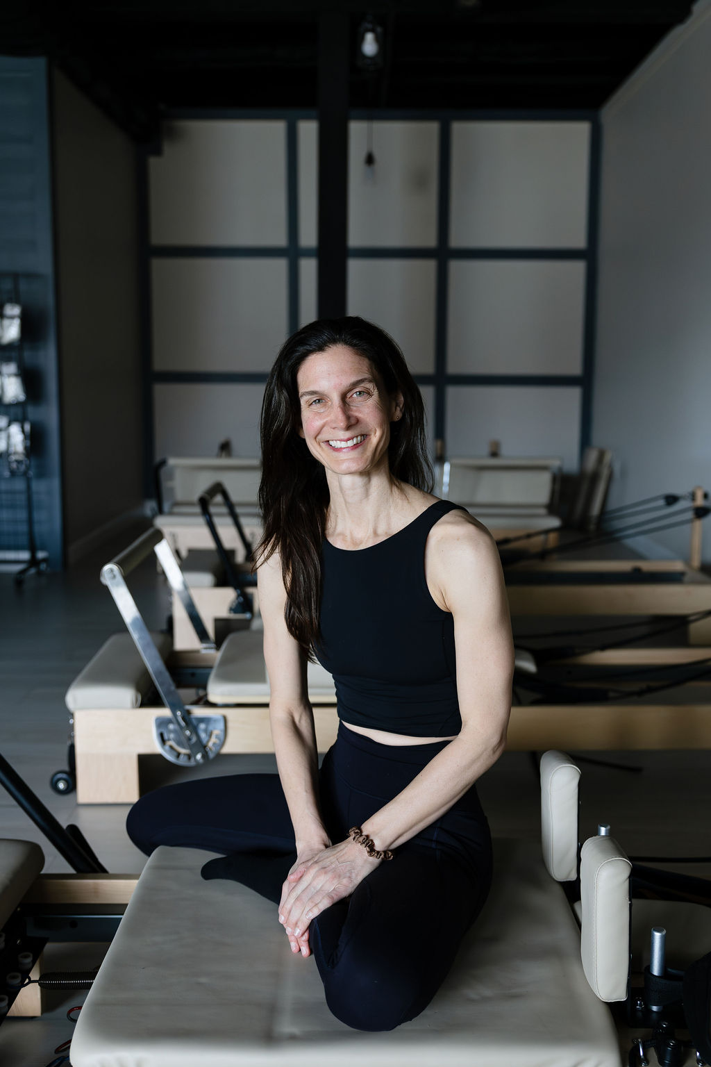 Alisa Willman seated on a Pilates reformer in her studio